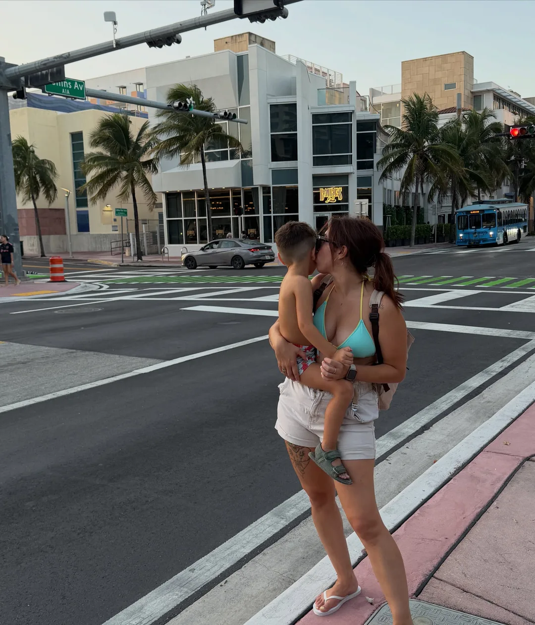 Yaiza con bikini azul y shorts blancos, sosteniendo a Nolan en una calle de Miami